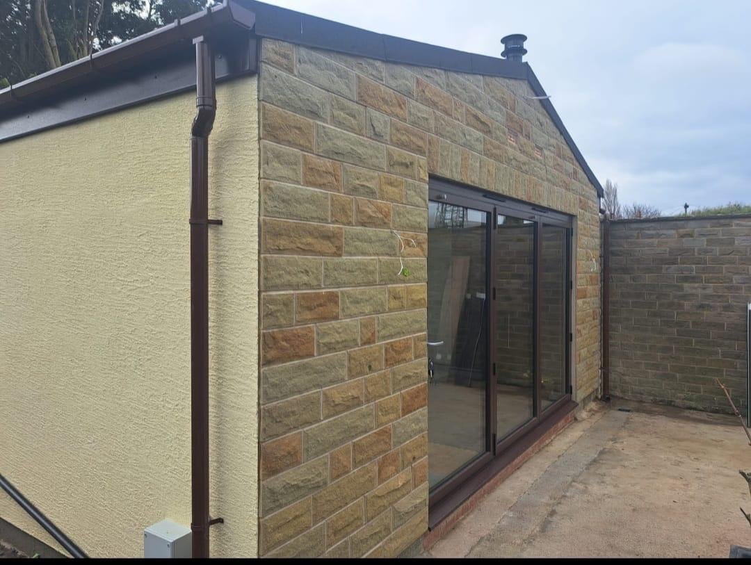 A completed single-storey extension with a rendered side wall, natural stone gable and full-height bi-fold doors onto a new patio.